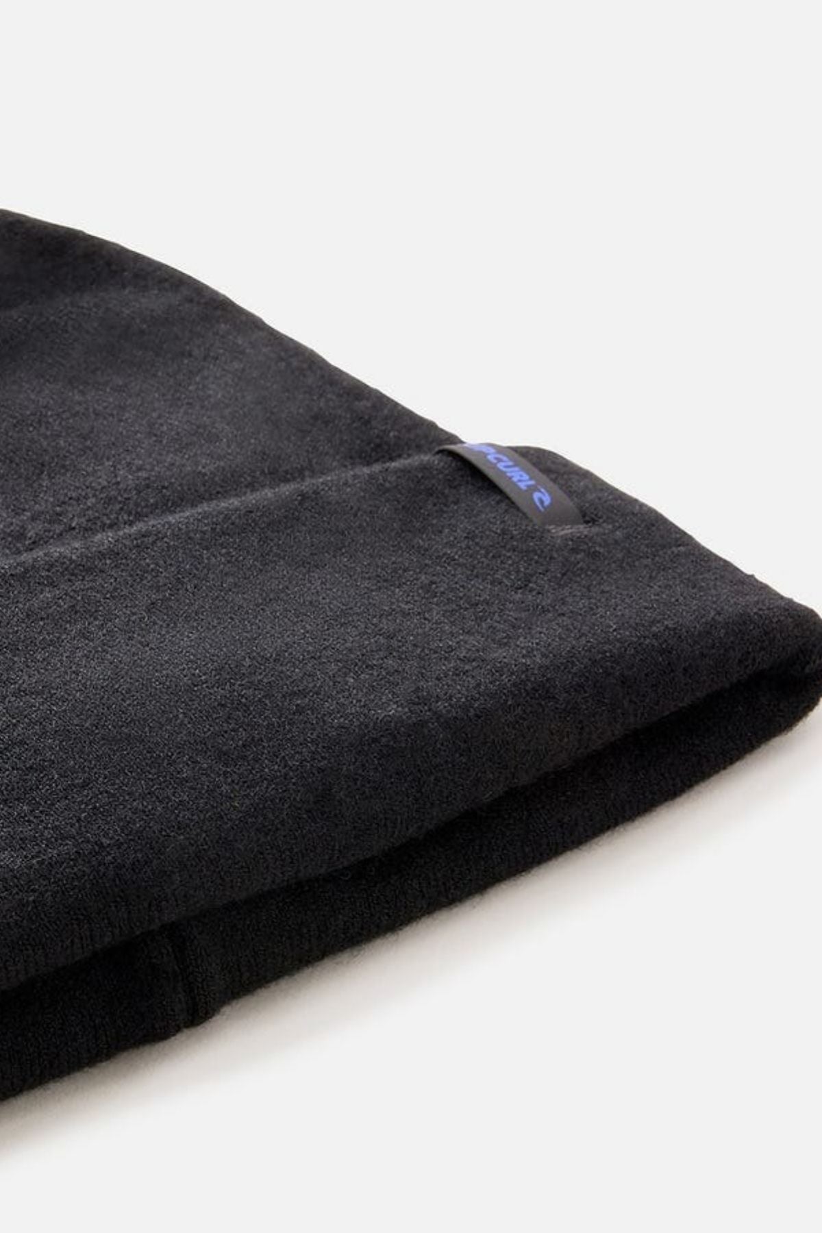 Close-up of a folded black Rip Curl Anti-Series Reg Tech Beanie featuring a small blue and white tag on the cuff, set against a plain light background—ideal for outdoor adventures.