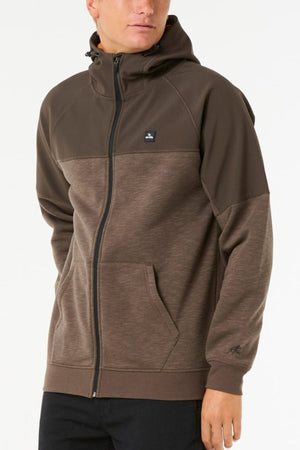 Wearing a Rip Curl Anti Series Viral Zip Thru hoodie—brown, zip-up, with a hood, front pockets, and subtle black chest logo—against a plain light background; ideal for stylish adventure wear.