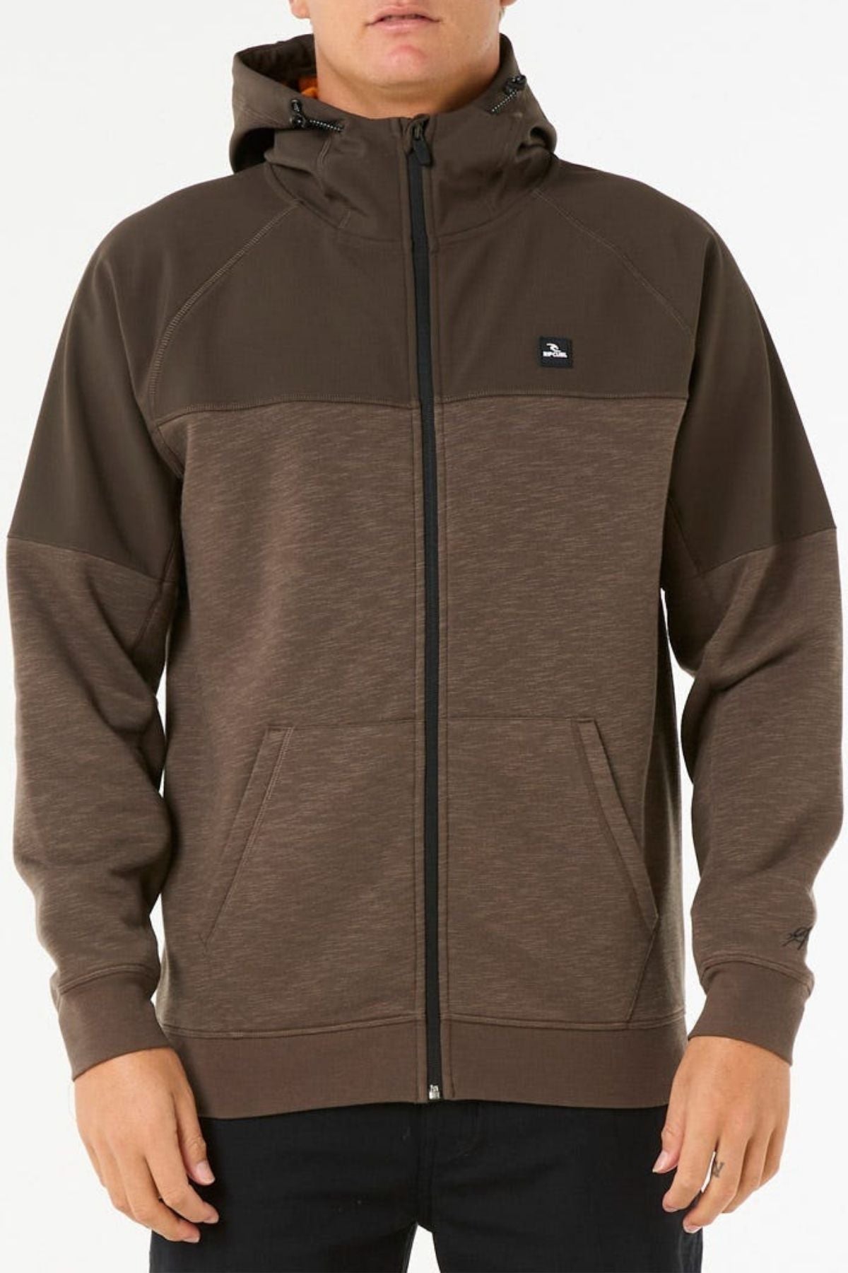 A person wearing a brown Rip Curl Anti Series Viral Zip Thru hoodie with a small chest logo, standing against a plain white background—ideal for anyone wanting stylish adventure wear.