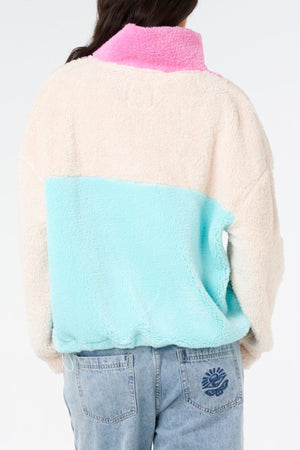 A person is seen from the back in a Rip Curl Block Party II Zip Through Polar Fleece, featuring a pink collar, cream top, and light blue bottom, styled with light blue jeans against a plain background.