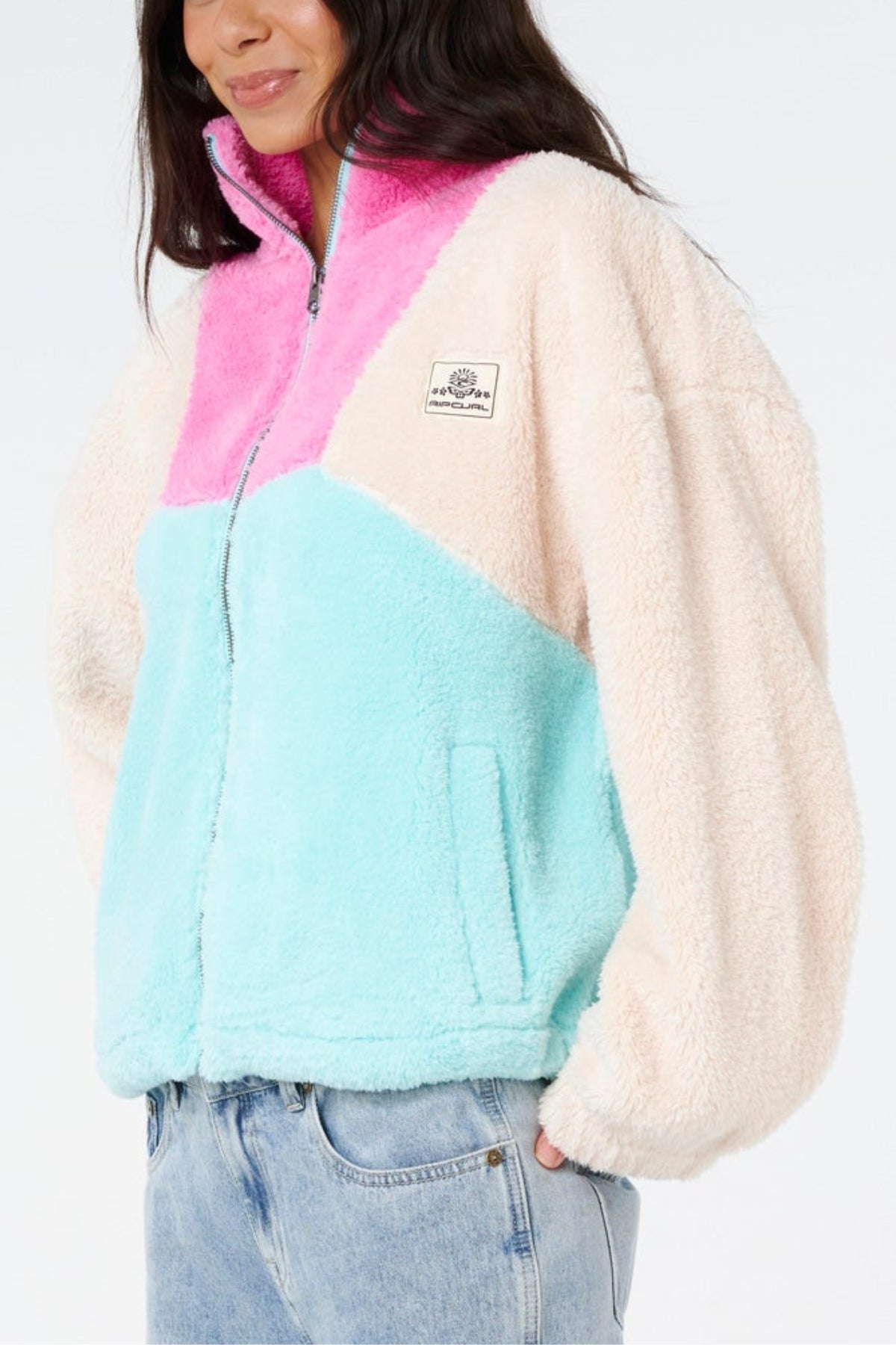 A person wearing the Rip Curl Block Party II Zip Through Polar Fleece with cream sleeves, a pink top, and light blue bottom, paired with light blue jeans—an ideal outfit for outdoor adventures.