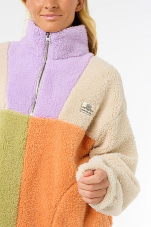Wearing a cozy Rip Curl Block Party Polar Fleece with lavender, beige, green, and orange panels, high zip-up collar, and chest patch; only the person’s lower face and upper body can be seen.