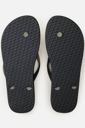 A pair of black Rip Curl Camo Bloom Thongs shown from the bottom, highlighting textured soles and the circular and oval plugs where straps attach. Crafted with BLOOM algae foam for comfort.