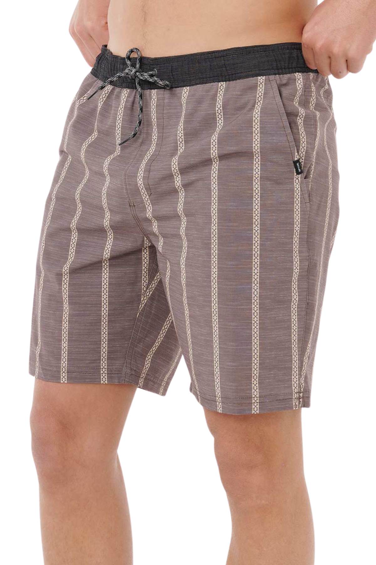 A person wearing Rip Curl Boardwalk Jackson Volley shorts in brown with beige vertical patterns and a black drawstring, hands in pockets. The image is cropped at the torso and knees.