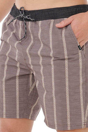 A person wears Rip Curl Boardwalk Jackson Volley boardshorts in brown with cream and patterned stripes, featuring a black waistband and drawstring. Quick-dry fabric; one hand in the pocket. Image is cropped waist to mid-thigh.