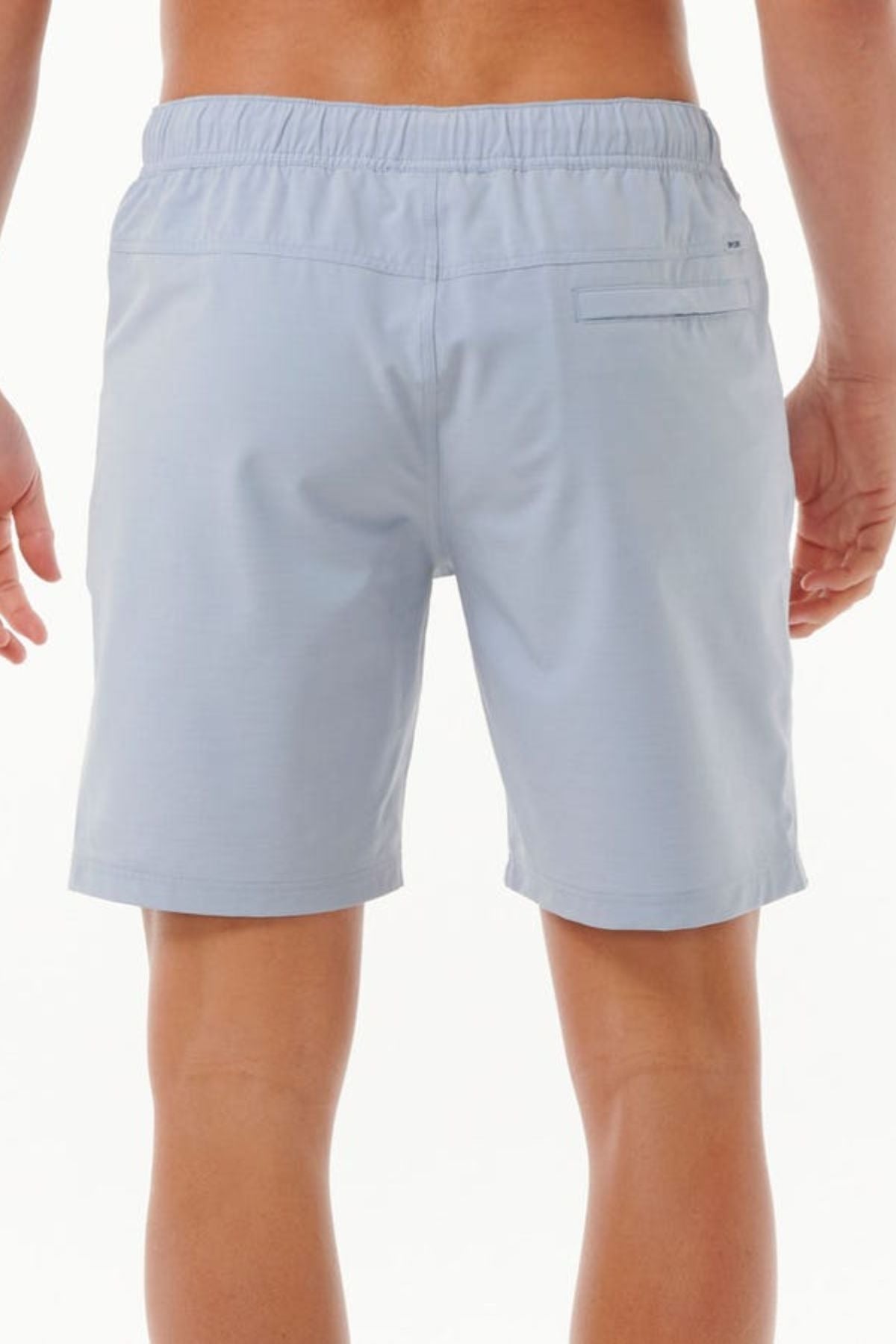 A person wearing Rip Curl Boardwalk Jackson Volley shorts in light blue is shown from the back. The shorts feature an elastic waistband and a single back pocket, crafted from quick-dry fabric. The person stands against a neutral background, ready for any adventure.