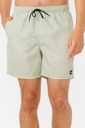 A person stands wearing light green Rip Curl Bondi Volley swim trunks, made from recycled PET, featuring a black drawstring. Their left hand rests in the pocket as they pose against a simple, light background.