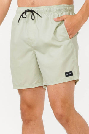 A person is seen wearing light green Rip Curl Bondi Volley shorts, featuring a black drawstring and the "Rip Curl" logo on the left side. Made from recycled PET, these eco-friendly board shorts are ideal for environmentally conscious beachgoers. The person stands with one hand in their pocket against a plain white background.