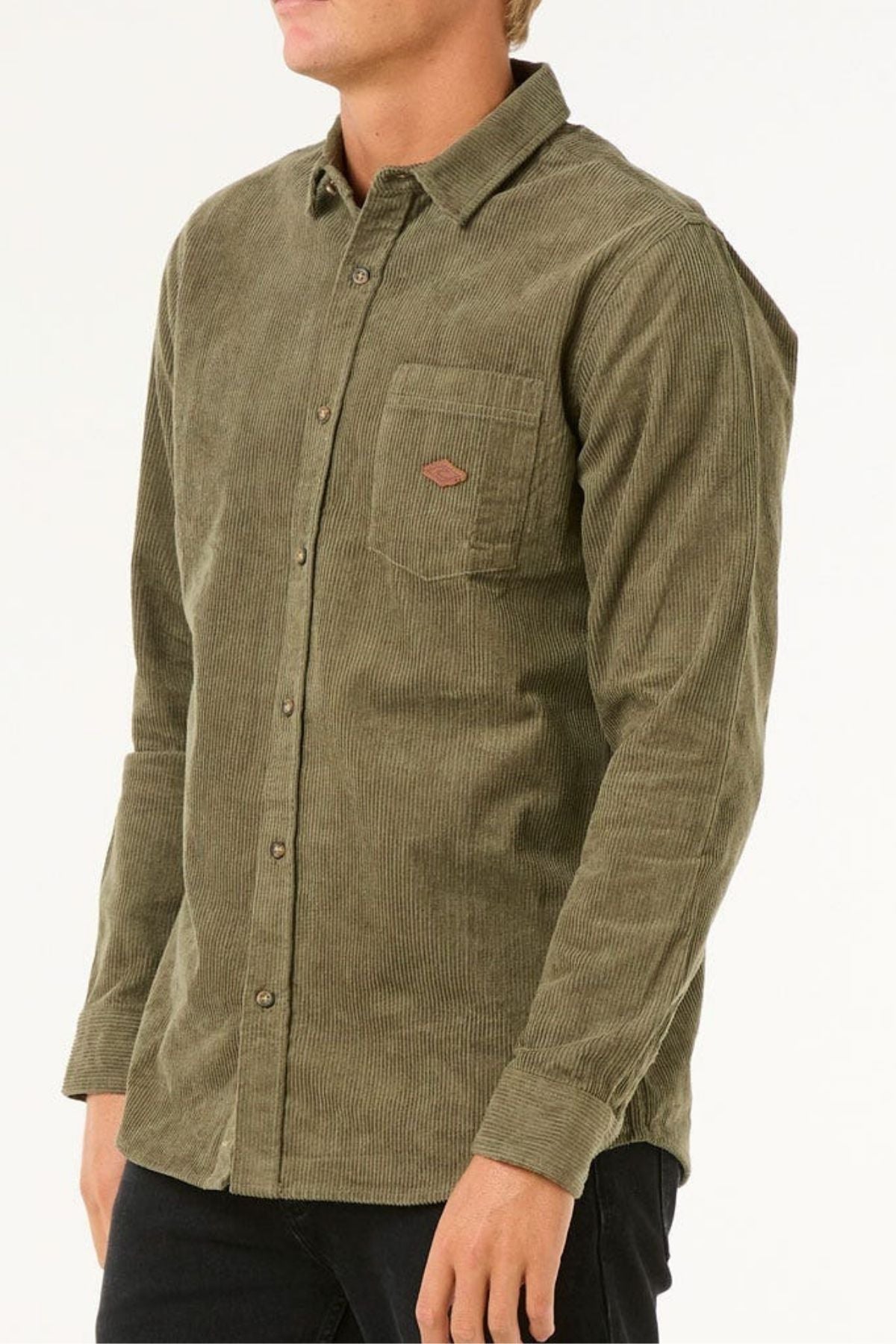 A person wears an olive green Rip Curl Classic Surf Cord Shirt with a chest pocket and black pants, standing against a plain light background.