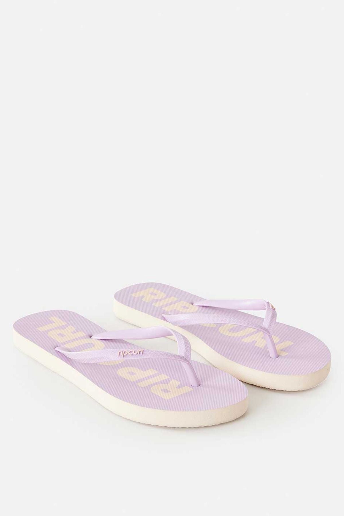The Rip Curl Classic Surf Bloom Thongs, featuring thin straps in light purple, are showcased on a plain background. Designed as sustainable footwear, the soles are crafted from BLOOM algae-blended foam and display the "Rip Curl" brand name in beige text. One sandal is positioned slightly ahead of the other.