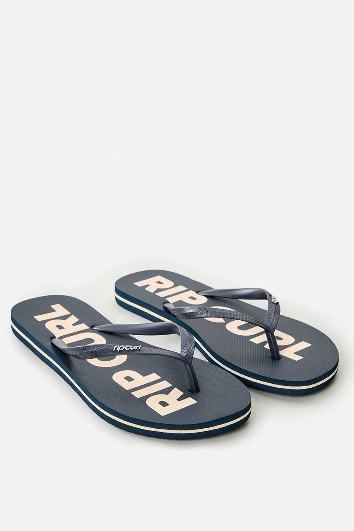 The Rip Curl Classic Surf Bloom Thongs in navy blue feature white "RIP CURL" lettering on the soles. They come with ergonomic molded straps and a textured footbed crafted from BLOOM algae-blended foam, diagonally positioned to prominently showcase the branding.