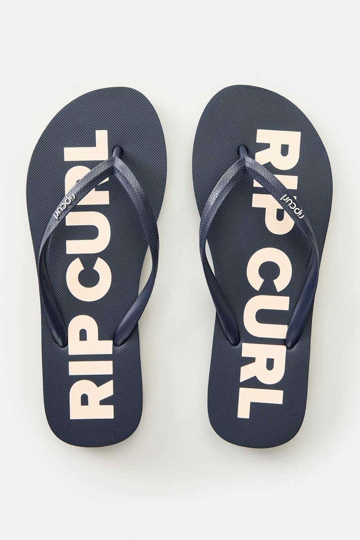 The Rip Curl Classic Surf Bloom Thongs feature ergonomic molded straps that complement a sleek black footbed adorned with "RIP CURL" in bold white letters. Made from BLOOM algae-blended foam, they offer a stylish and sustainable option for any plain backdrop.