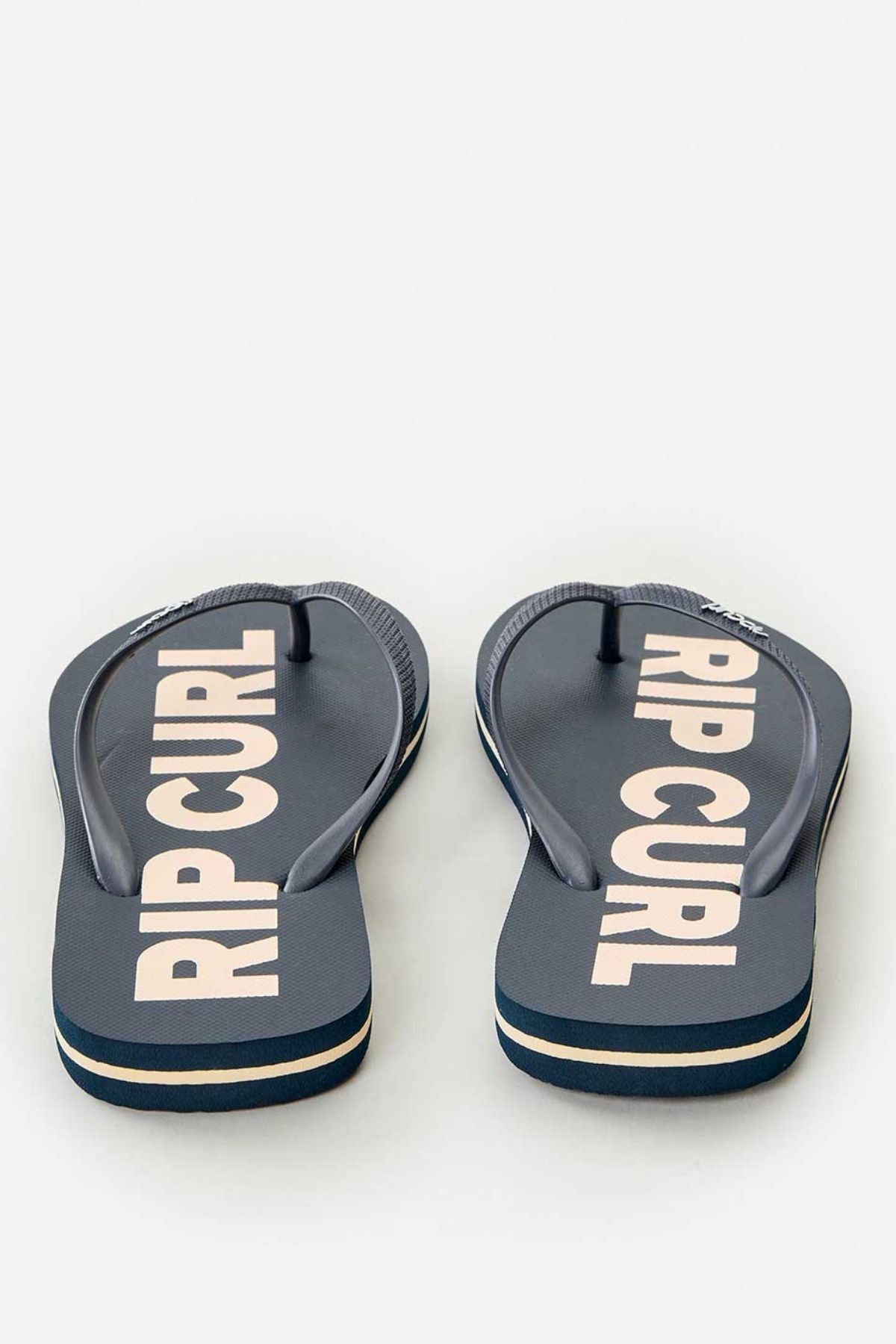 The Rip Curl Classic Surf Bloom Thongs in dark gray showcase ergonomic molded straps and prominently display the brand name in bold white letters on the footbed. Crafted with BLOOM algae-blended foam, they stand out stylishly against a light background.