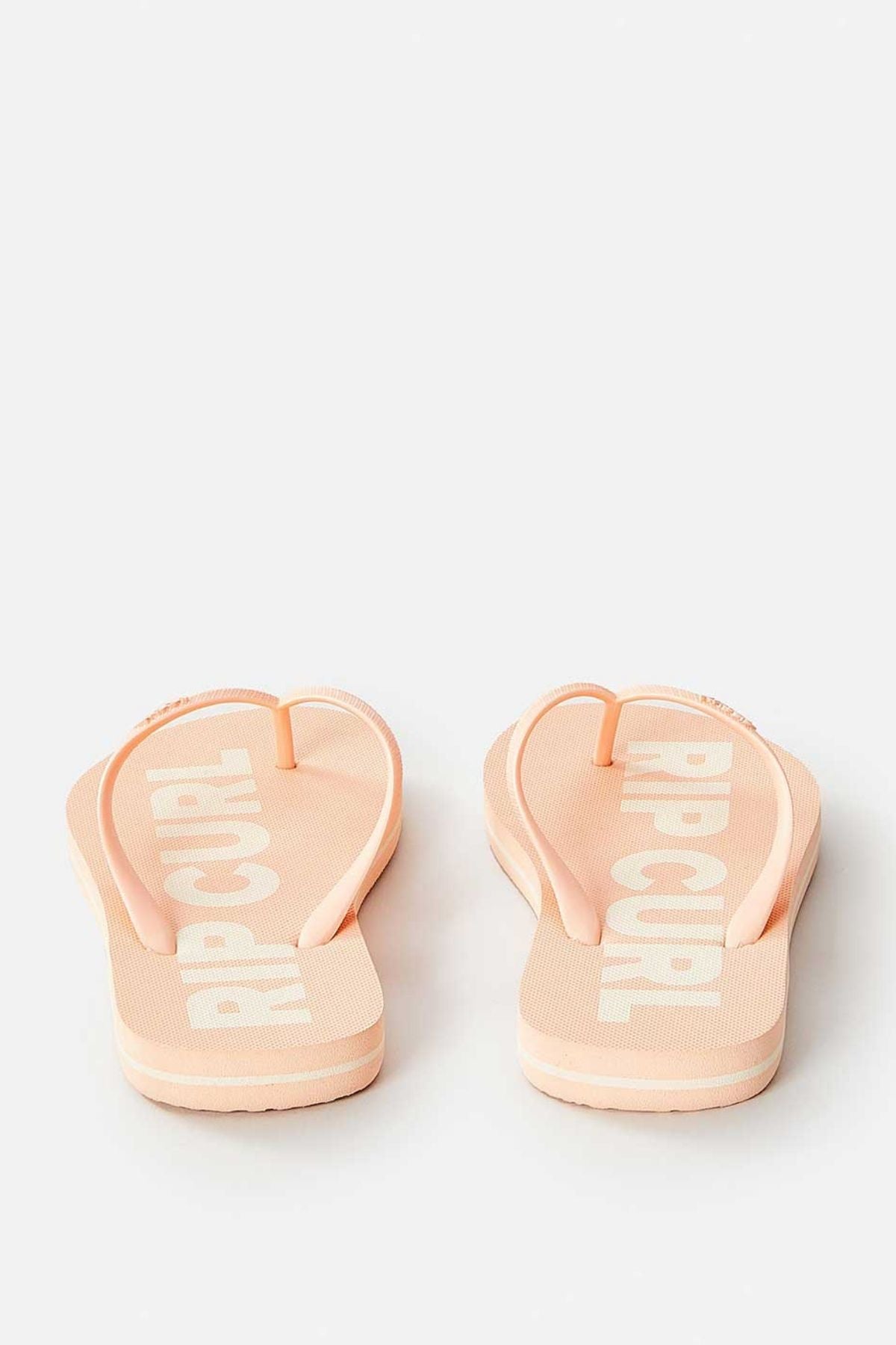 A pair of Rip Curl Classic Surf Bloom Thongs in pale pink, crafted for sustainable comfort with BLOOM™ algae-blended foam EVA, and showcasing white text on the footbed, is displayed from the back against a plain background.