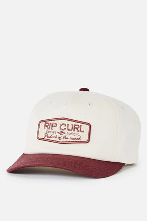 The Rip Curl Classic Surf SB Cap is a white cotton snapback hat featuring a maroon brim and a maroon embroidered patch on the front that reads “RIP CURL Surfing Co. Product of the Search,” capturing timeless surf culture style.