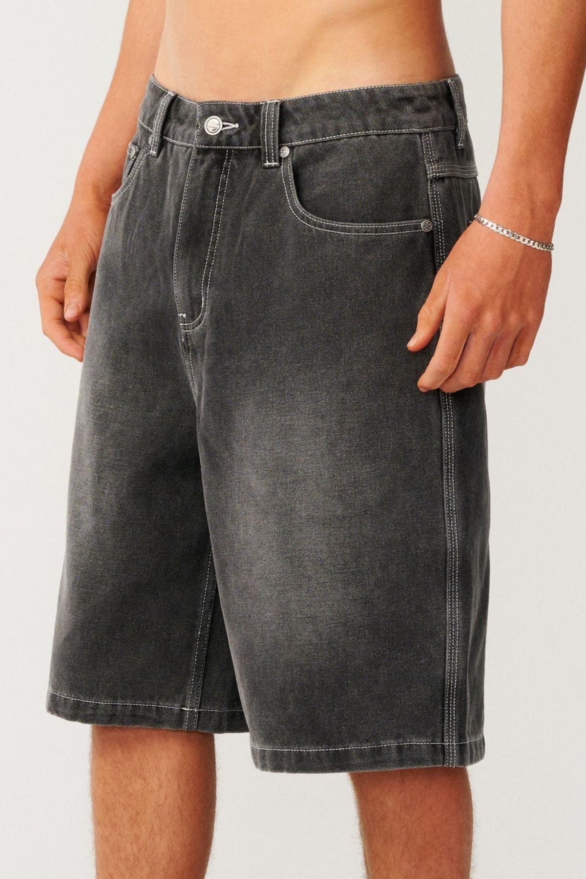 A person wearing relaxed, baggy charcoal grey Rip Curl Archive Dirty Denim Walkie Walkshort with white contrast stitching.