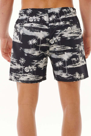 A person wearing the Rip Curl Dreamers Volley board shorts, showcasing a white tropical palm tree pattern on a black background, is standing with their back to the camera. Made from recycled fabric, these shorts feature an all-over print against a plain, light background.