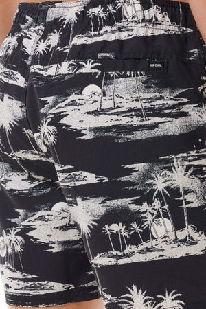 Close-up of the Rip Curl Dreamers Volley board shorts in black and white, showcasing an all-over print of a tropical beach scene with palm trees, clouds, and a setting sun. Crafted from recycled fabric, the back pocket features a tag that reads "Rip Curl.