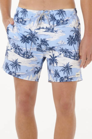 Wearing the Rip Curl Dreamers Volley shorts in light blue with a white and navy tropical island and palm tree print, a person stands against a plain backdrop with their left hand in their pocket, highlighting this stylish, sustainable swimwear.