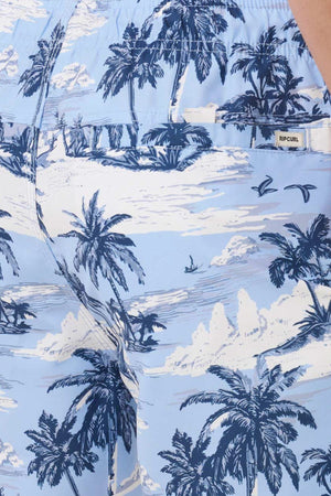 Close-up of Rip Curl Dreamers Volley shorts in light blue, with a white and navy tropical island print of palm trees, birds, and waves; quick-dry fabric and a small "RIP CURL" tag by the back pocket.