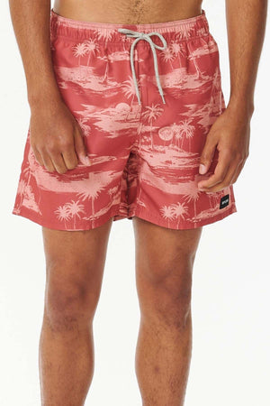 A person wearing the Rip Curl Dreamers Volley, which are stylish pink board shorts adorned with a tropical palm tree pattern, stands against a plain white background. The shorts, crafted from recycled fabric, feature a sleek white drawstring.