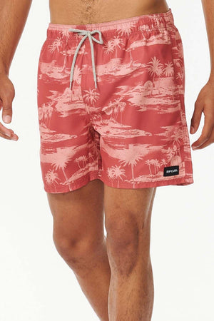 A person is wearing Rip Curl Dreamers Volley board shorts in coral, featuring a stylish tropical print with palm trees and island scenery. Made from recycled fabric, these shorts include a drawstring and a small brand patch on the left leg, set against a plain white background.