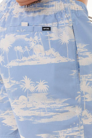 Close-up of stylish above-the-fit light blue "Rip Curl Dreamers Volley" board shorts, adorned with a white tropical print featuring palm trees and island scenes. Crafted from recycled rip suede fabric, these shorts are finished with a black label reading "RIPCURL" on the waistband, enhancing the beach vibe with their soft texture and vibrant print.