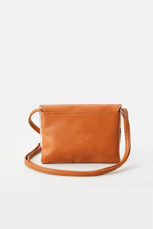 The Rip Curl Essentials II Festival Bag, a small rectangular crossbody bag made from tan leather with an adjustable shoulder strap, is set against a plain, light backdrop. Its simple design and textured leather surface make it ideal for any outing.