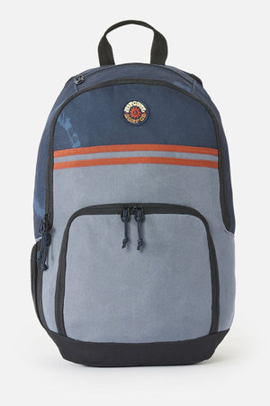 Blue two-tone Rip Curl Evo 24L Rinsed Backpack with a front zip pocket, two horizontal orange stripes, and a circular logo patch near the top.