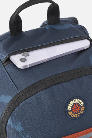 Close-up of a blue patterned Rip Curl Evo 24L Rinsed Backpack featuring a zippered insulated cooler pocket with a smartphone tucked inside and a circular logo patch.