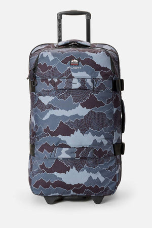 The Rip Curl F-Light Global 100L Search Camo Travel Bag with wheels, retractable handle, blue and gray camo pattern in recycled polyester, and black straps stands upright against a plain white background.