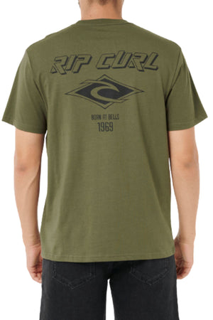 A person wearing a relaxed fit olive green Rip Curl Fade Out Icon Tee is seen from the back, featuring a large black Rip Curl logo and “RIP CURL BORN AT BELLS 1969” on the upper back for classic throwback vibes.