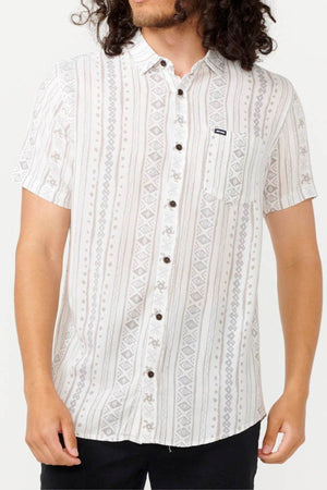 A person is wearing the Rip Curl Fun Times Short Sleeve Shirt, crafted from eco-friendly material and featuring a light-colored geometric pattern with a small chest pocket on the left. It's paired with dark pants, creating a casual vibe ideal for laid-back outings.