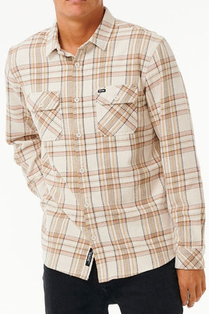 A person wears the Rip Curl Griffin Flannel Shirt—beige and brown plaid cotton flannel with two front pockets—standing against a plain white background.