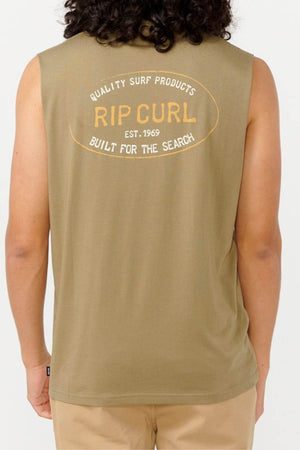 The individual with long hair is sporting the Rip Curl Hallmark Muscle, an olive green muscle fit sleeveless shirt. Crafted from 100% cotton, it displays a "Rip Curl" logo along with the text "Quality Surf Products, Rip Curl, Est. 1969, Built for the Search" on the back while facing away from the camera.