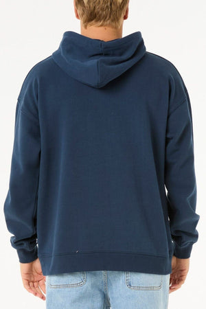 A person is seen from behind wearing a Rip Curl Heritage Oval Hood in dark blue with light blue jeans, standing against a plain white background.
