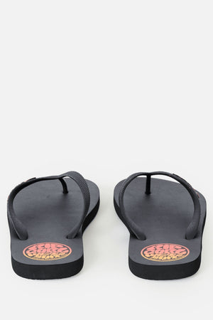 A pair of Rip Curl Icons Of Surf Bloom Open Toe Sandals with thin black straps and a round orange and yellow logo on the heel area, crafted from eco-friendly BLOOM algae foam, displayed on a plain white background.
