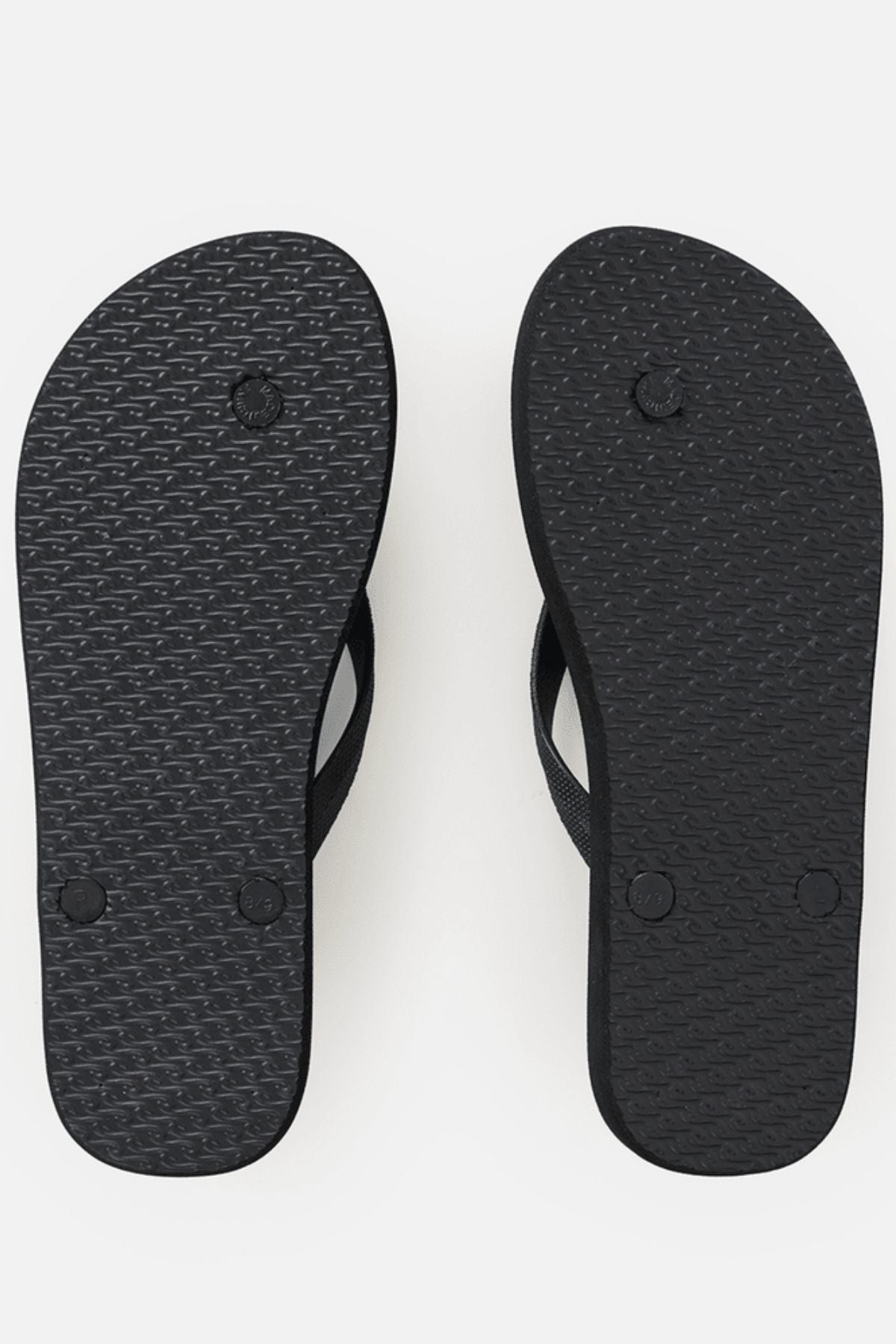 A pair of Rip Curl Icons Of Surf Bloom Open Toe Sandals are shown with the soles facing up, revealing a textured pattern and visible circular strap attachments against a white background. Crafted from eco-friendly BLOOM algae foam, these sandals combine style with sustainability.