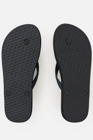 A pair of Rip Curl Icons Of Surf Bloom Open Toe Sandals are shown with the soles facing up, revealing a textured pattern and visible circular strap attachments against a white background. Crafted from eco-friendly BLOOM algae foam, these sandals combine style with sustainability.