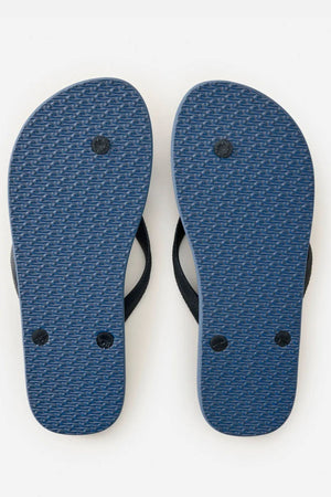 A pair of Rip Curl Icons of Surf Bloom Thongs in blue with black straps, shown from the bottom to highlight textured soles and circular plugs, crafted from eco-friendly BLOOM algae-blended foam, displayed on a white background.