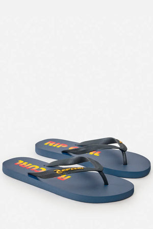 The Rip Curl Icons of Surf Bloom Thongs feature blue footbeds with dark straps and a yellow, red, and orange logo. Made with eco-friendly BLOOM algae-blended foam, they're shown on a light grey background.