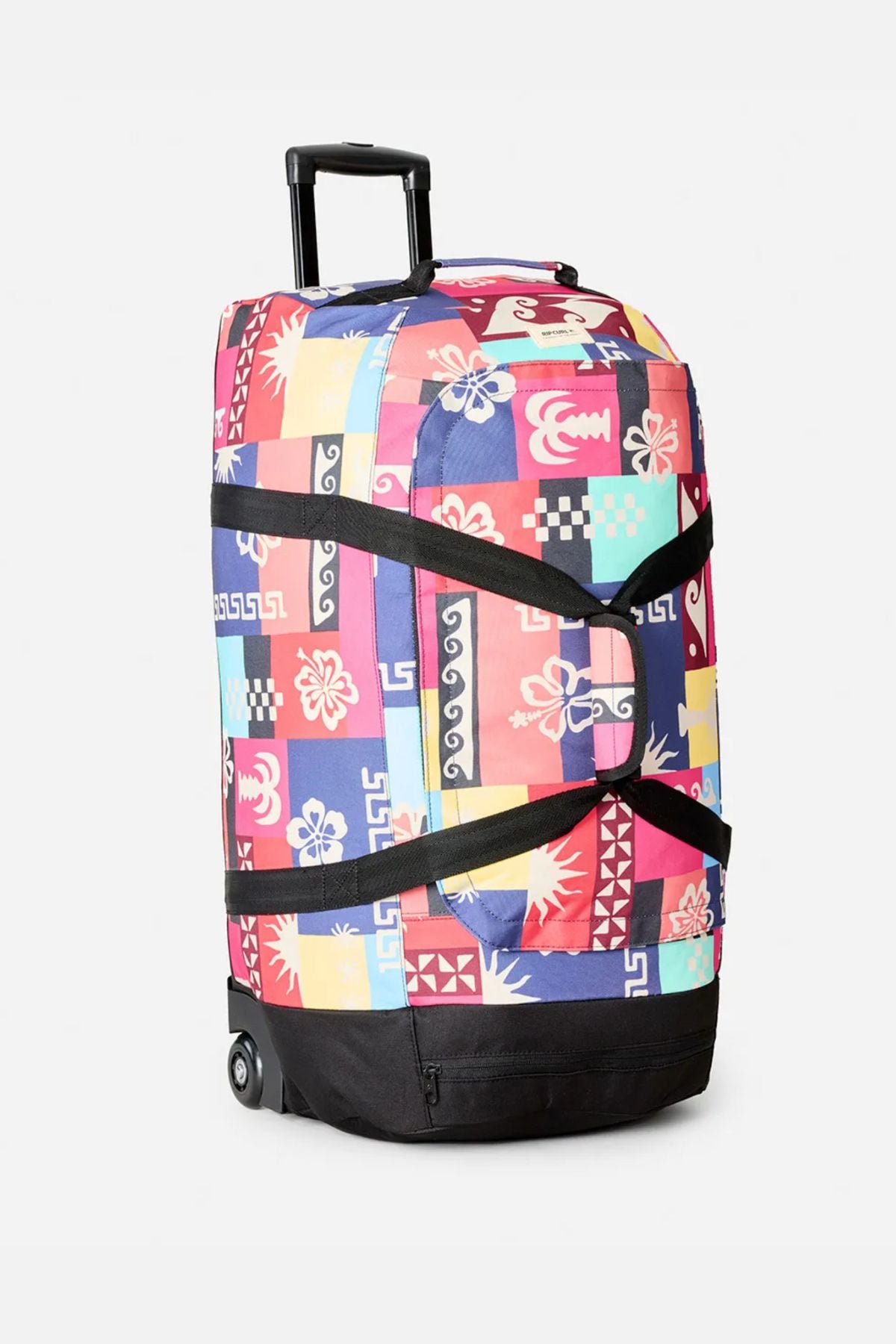 The Rip Curl Jupiter 80L Mixed Travel Bag is a rolling duffel with a pink, red, blue, and yellow geometric floral patchwork design, black straps, retractable handle, two wheels, and made from recycled polyester.