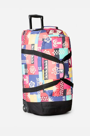 The Rip Curl Jupiter 80L Mixed Travel Bag is a rolling duffel with a pink, red, blue, and yellow geometric floral patchwork design, black straps, retractable handle, two wheels, and made from recycled polyester.