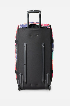 The Rip Curl Jupiter 80L Mixed Travel Bag stands upright on two wheels with an extended handle. Its back panel is plain black, and the sides feature colorful patterned fabric for a stylish look.