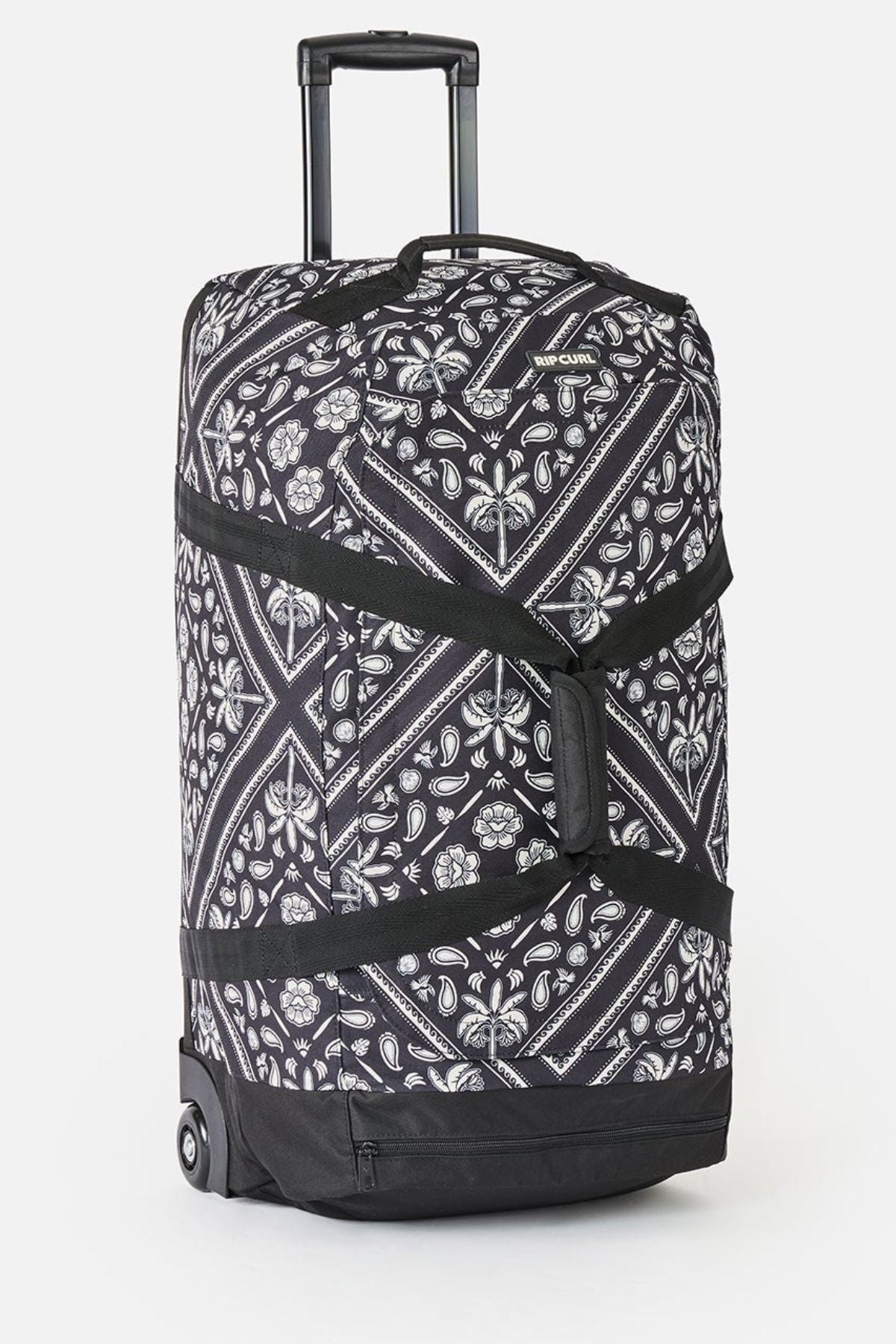 The Rip Curl Jupiter 80L Mixed Travel Bag is black and white with floral and geometric patterns, made from recycled polyester. It features two wheels, a telescoping handle, black straps, and an 80L capacity.