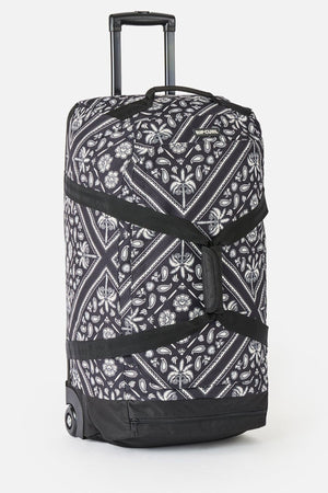 The Rip Curl Jupiter 80L Mixed Travel Bag is black and white with floral and geometric patterns, made from recycled polyester. It features two wheels, a telescoping handle, black straps, and an 80L capacity.