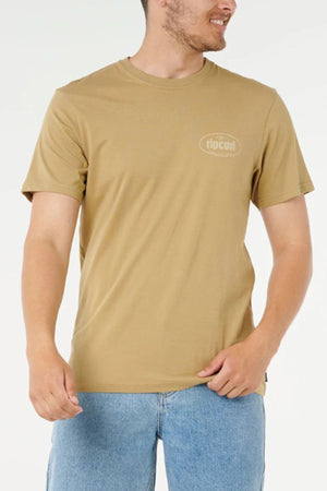 A man wearing a beige Rip Curl Everyday Tee and light blue jeans stands against a plain white background, looking to his left and smiling.