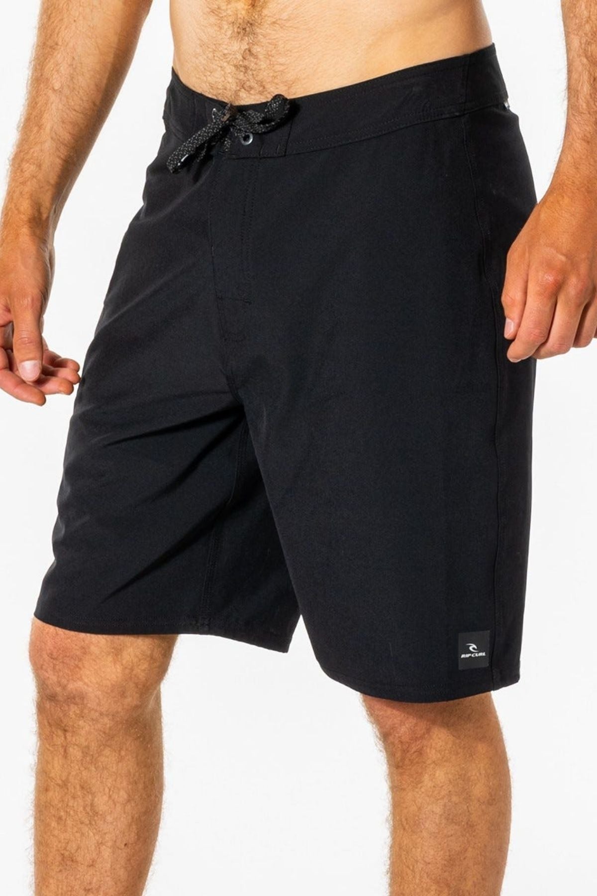 A man wearing black Rip Curl Mirage Core Boardshorts with a drawstring waist, standing against a plain white background.
