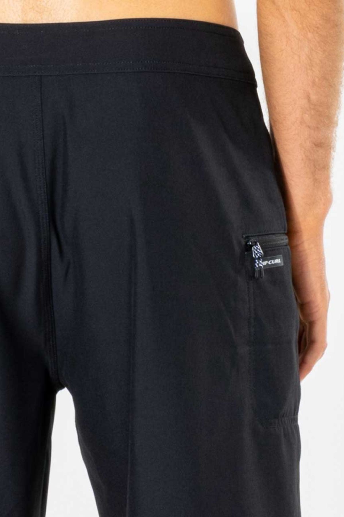 A close-up of the back of a person wearing the Rip Curl Mirage Core Boardshort, highlighting a small zippered right-side pocket with a visible pull tag and detailed stitching.