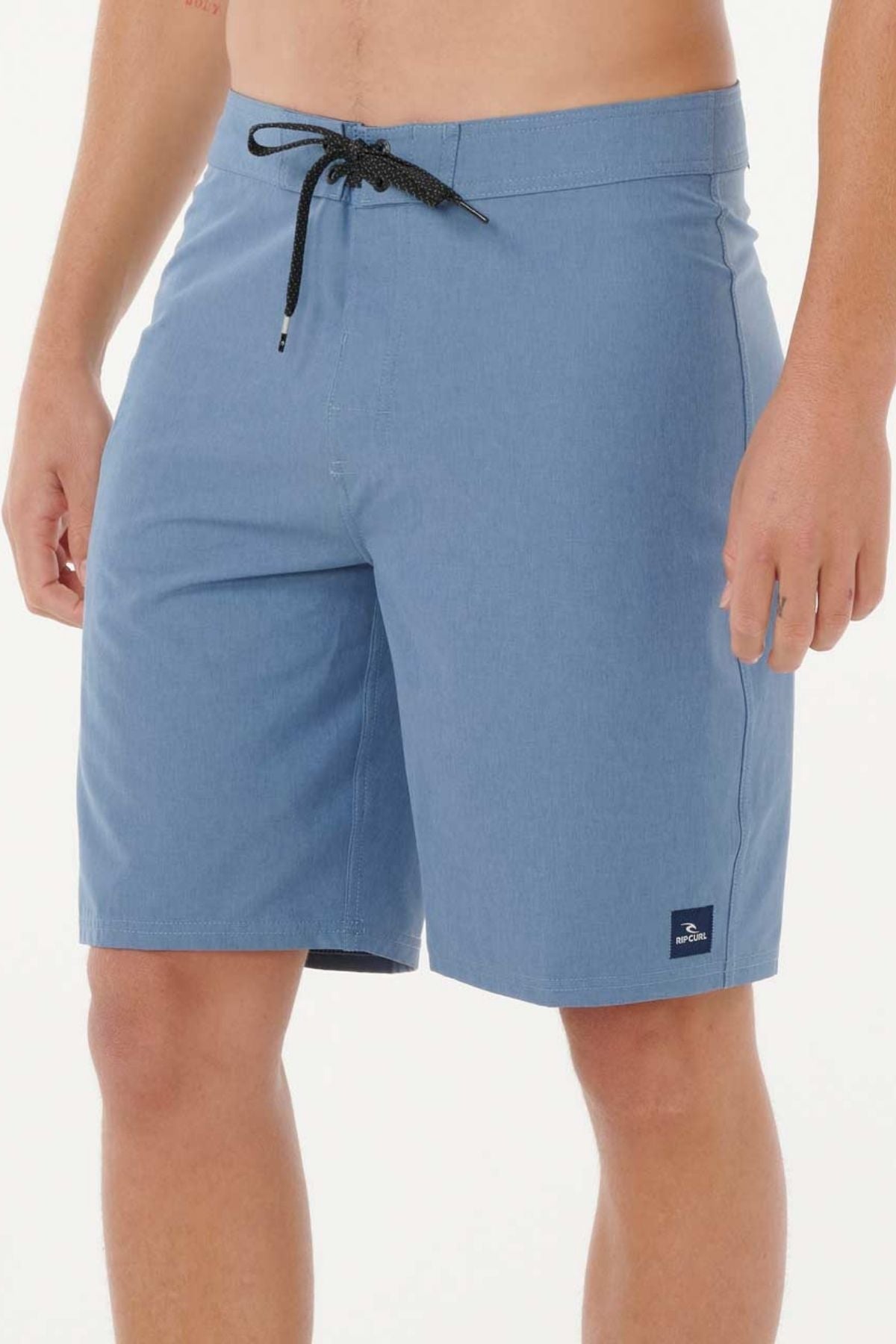 A person wearing light blue Rip Curl Mirage Core Boardshorts stands against a plain white background. The quick-dry shorts feature a small dark logo patch near the bottom hem.